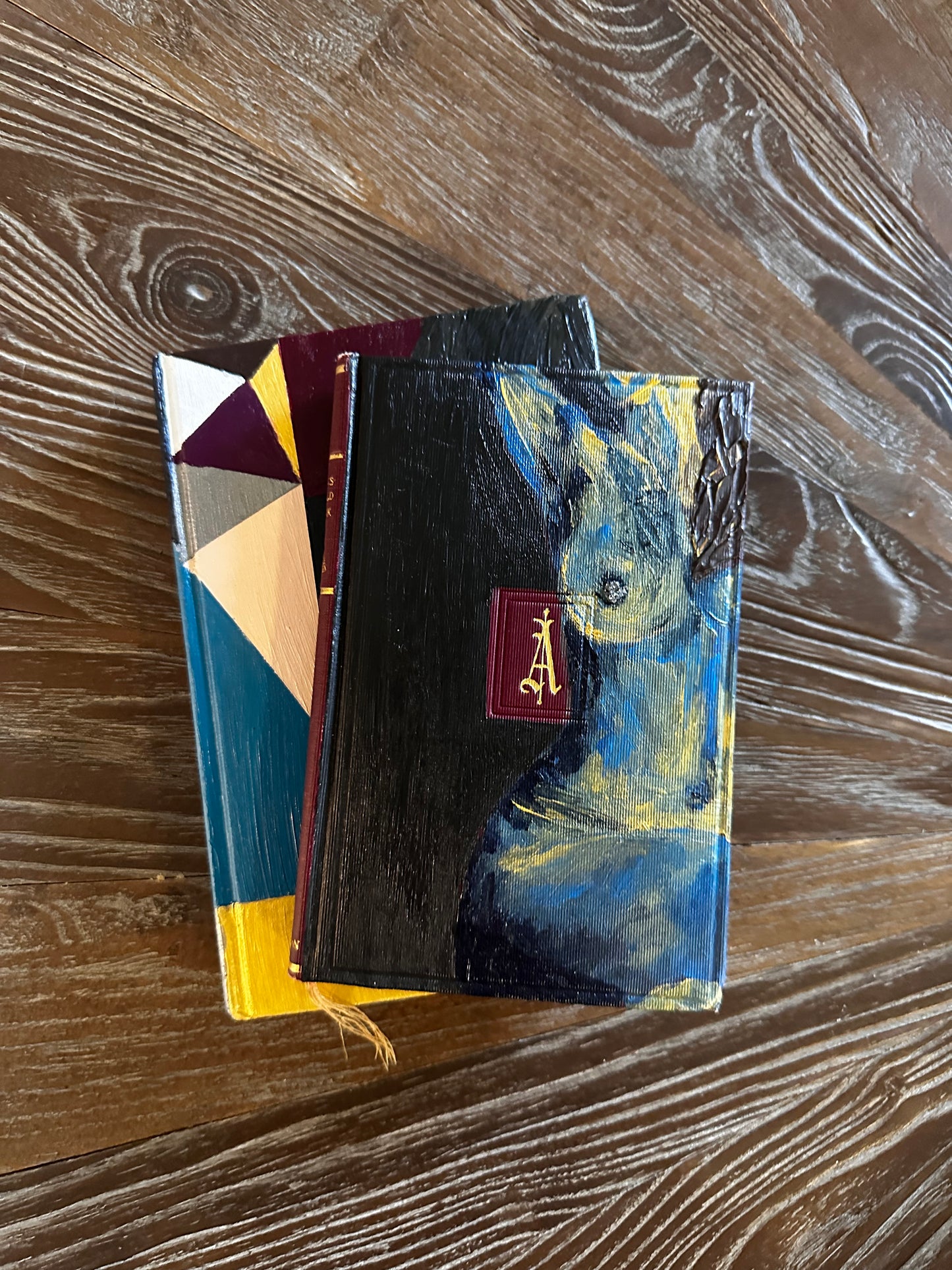 Stack of books with a black cover featuring a painting on a wooden surface